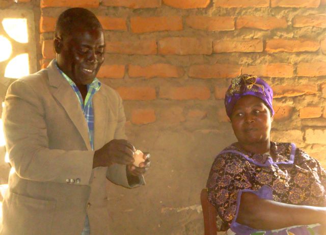 He asks the Group Village Headman at the end of the semi circle to peel the egg. The lady watching is the Traditional Authority (TA). 